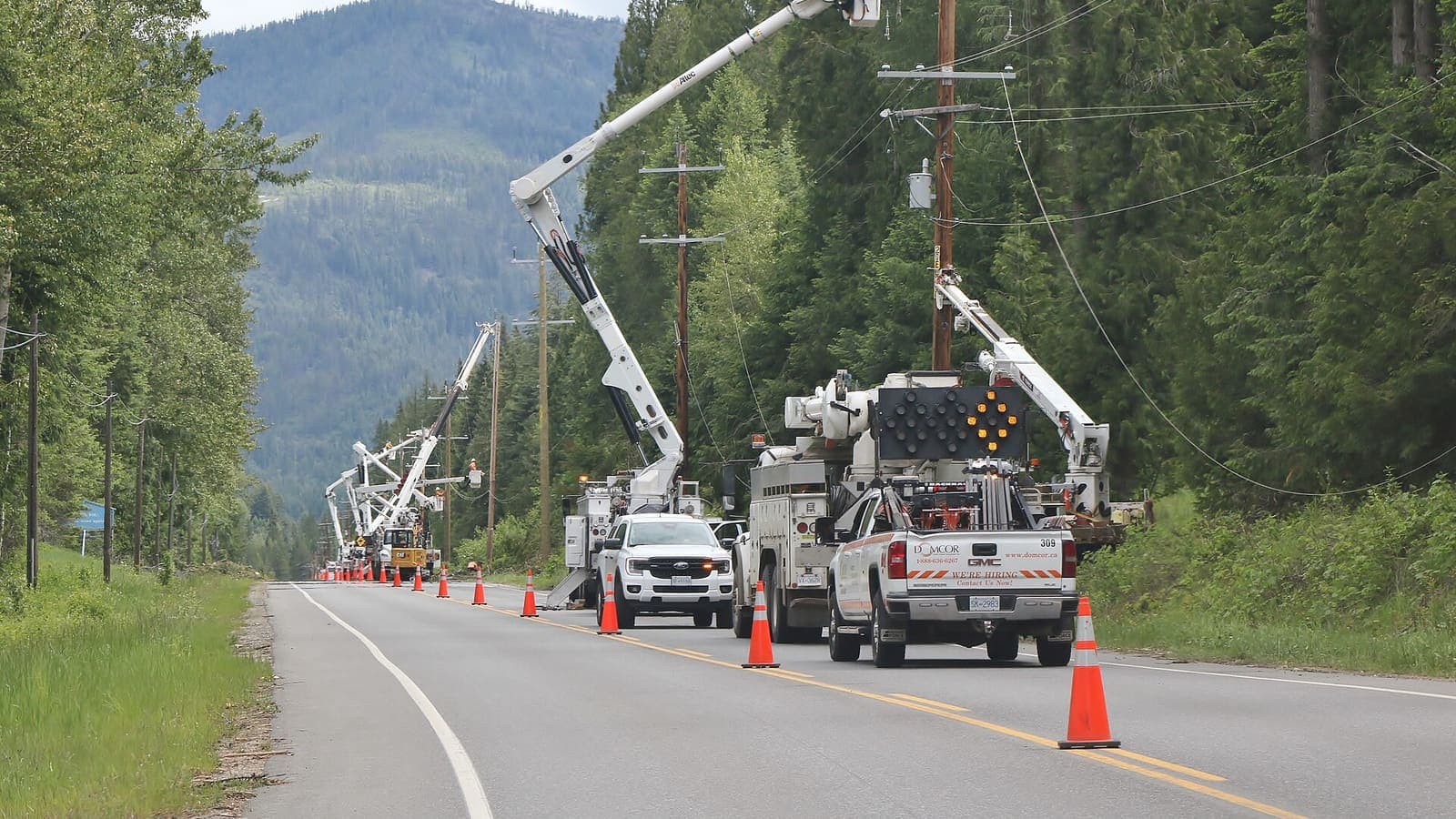 Utility crews in bucket trucks working on power lines along a highway near Fruitvale, British Columbia