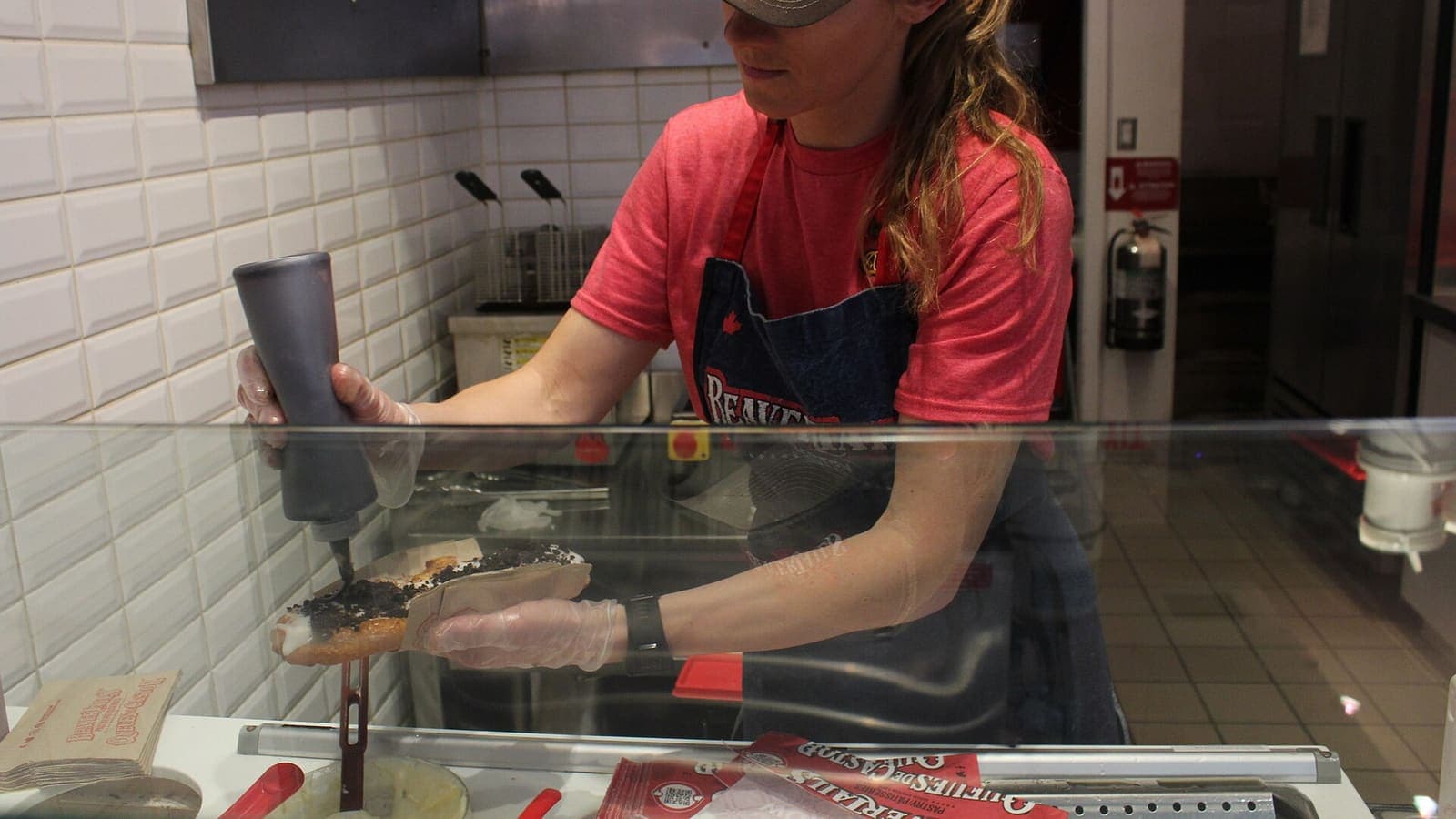 Un membre du personnel de BeaverTails étale une garniture sur une pâtisserie derrière le comptoir, à Banff, en Alberta